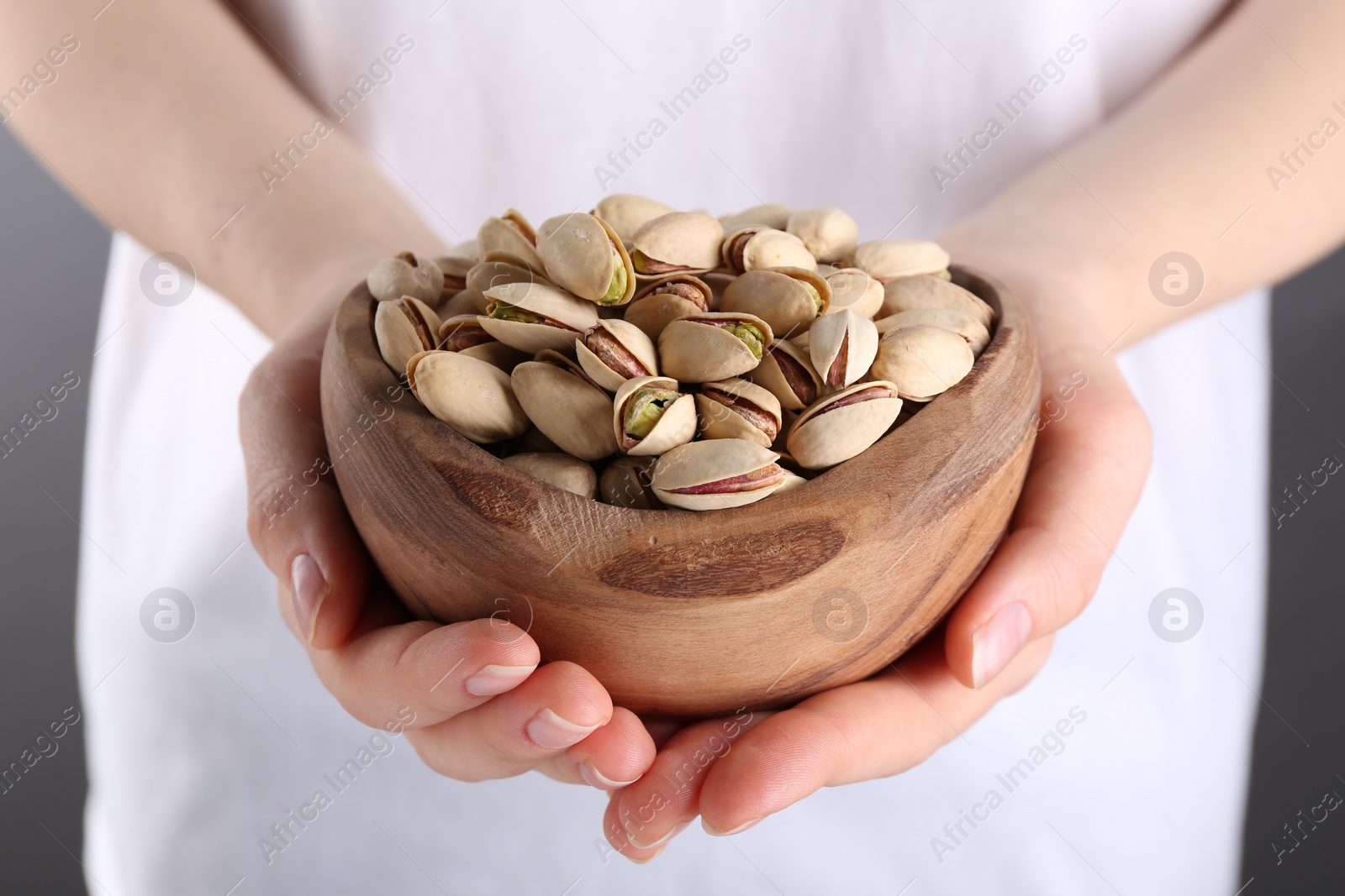 Photo of Woman holding tasty pistachios in bowl on grey background, closeup