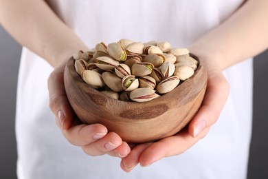 Photo of Woman holding tasty pistachios in bowl on grey background, closeup