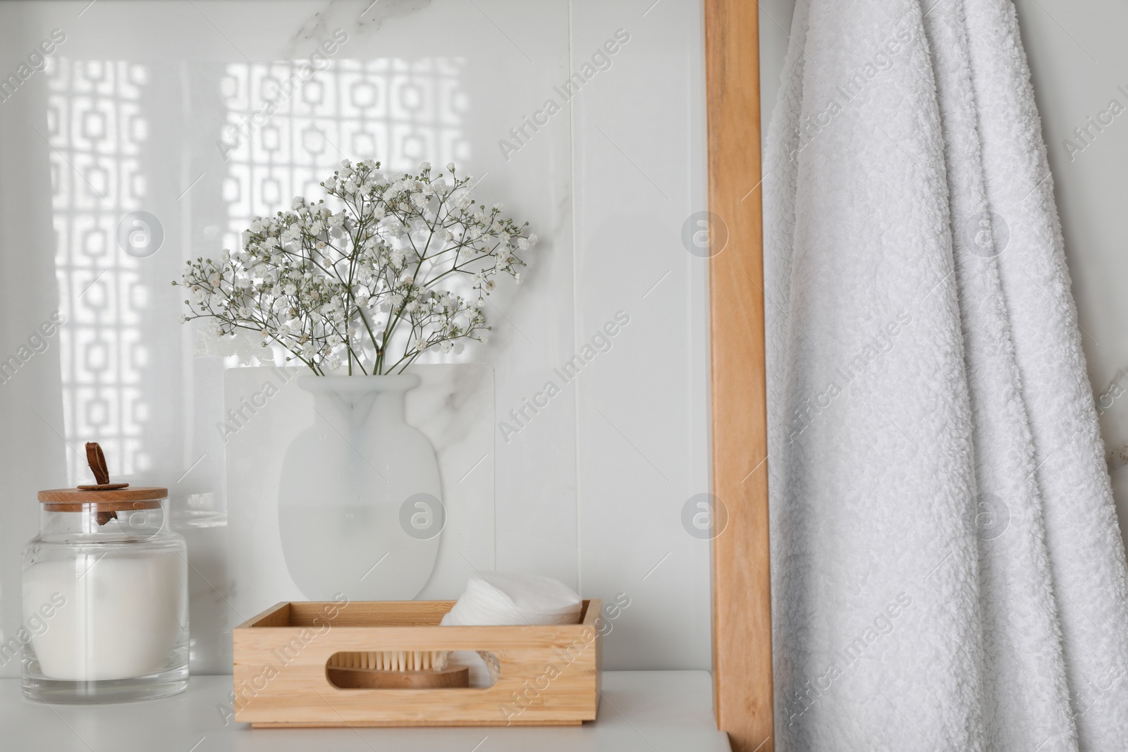 Photo of Silicone vase with flowers on white marble wall and shelving unit in stylish bathroom