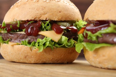 Photo of Delicious cheeseburgers with lettuce, pickle, ketchup and patty on wooden table, closeup