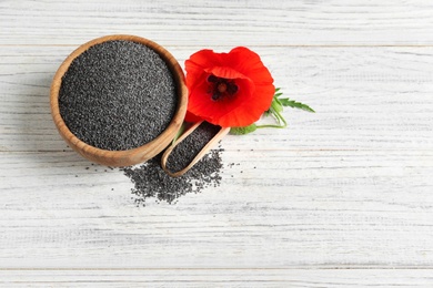 Photo of Wooden bowl of poppy seeds, scoop and flower on white table, above view with space for text