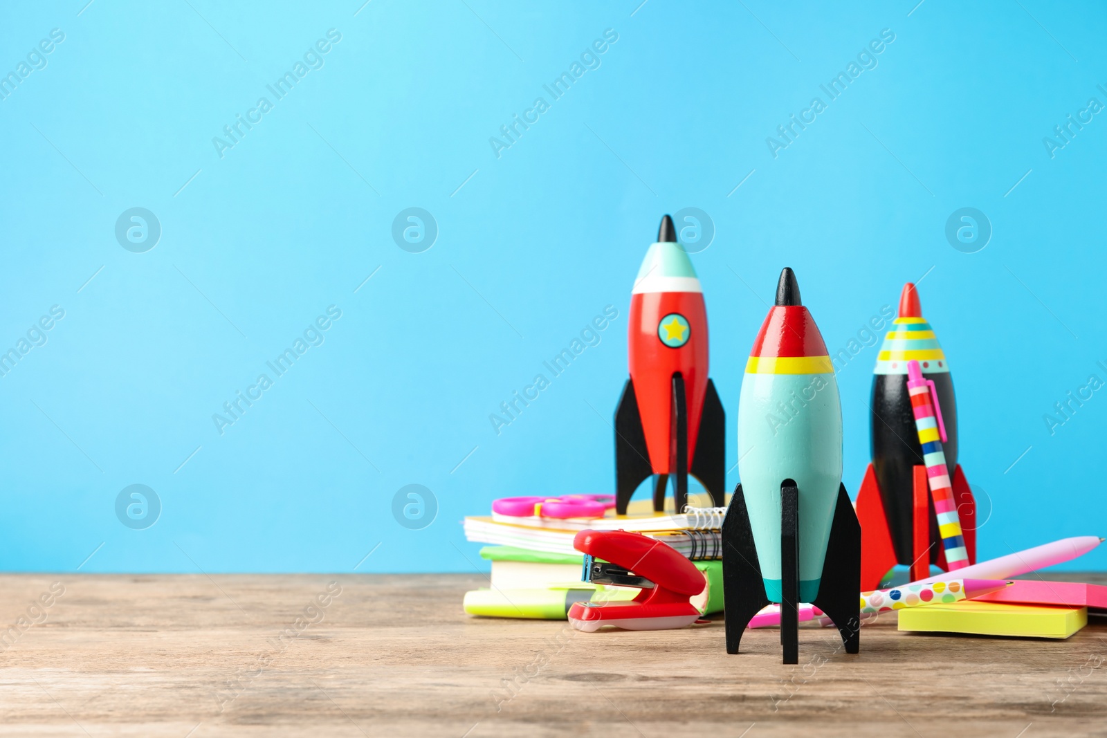 Photo of Bright toy rockets and school supplies on wooden table. Space for text