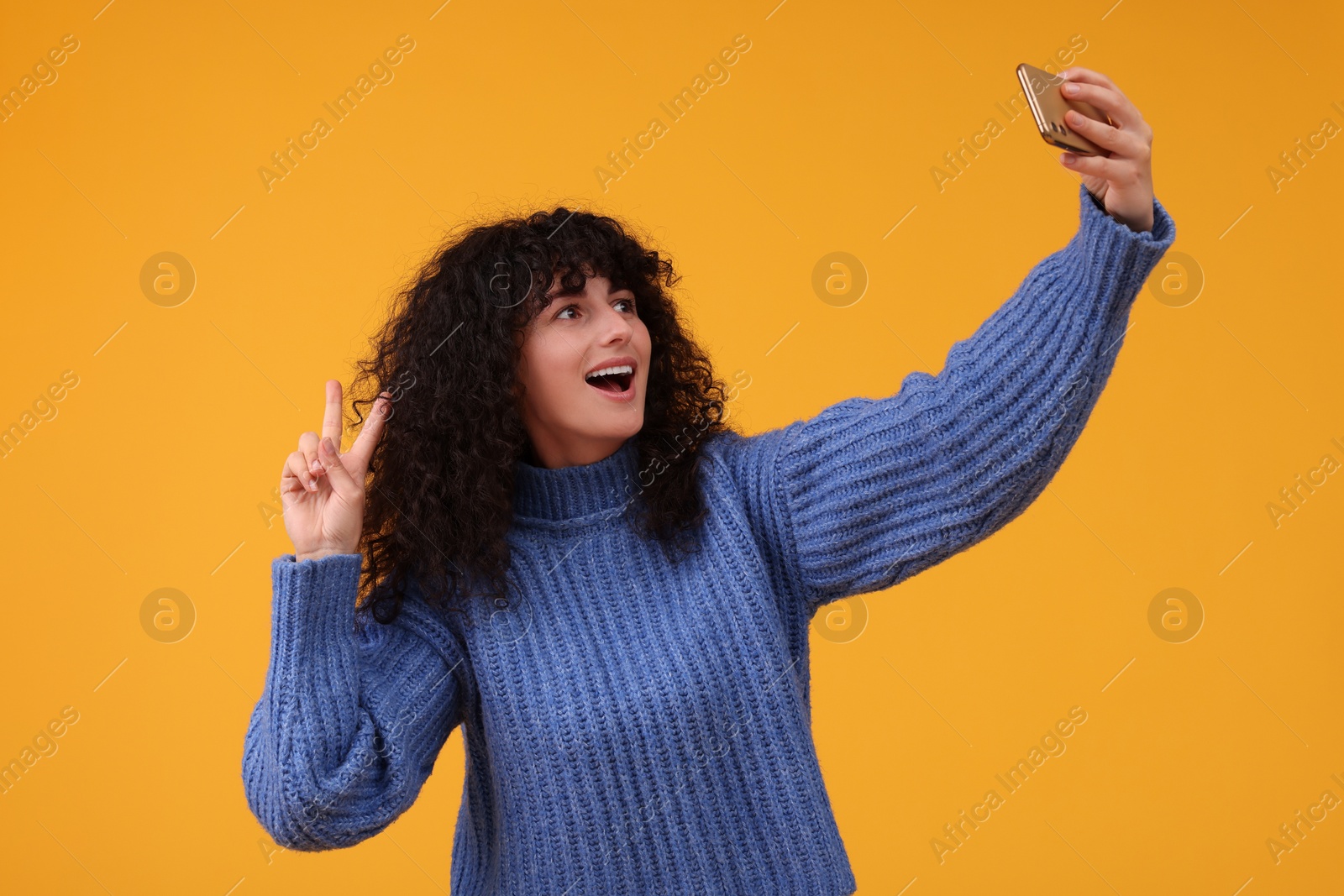 Photo of Beautiful young woman taking selfie with smartphone on orange background