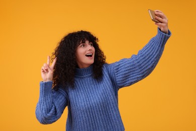 Beautiful young woman taking selfie with smartphone on orange background