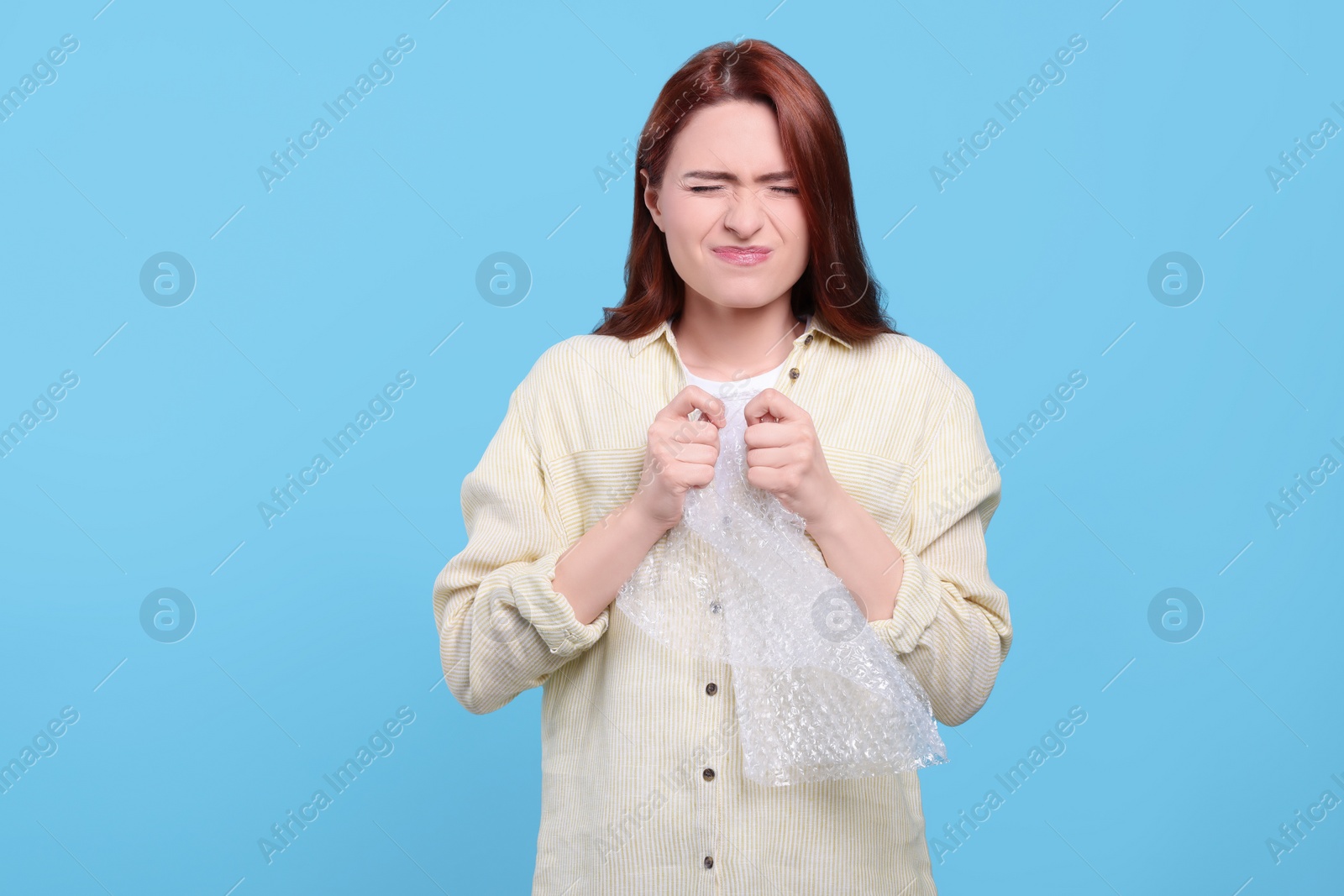 Photo of Angry woman popping bubble wrap on turquoise background. Stress relief