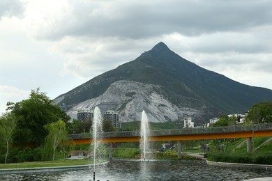 Photo of Beautiful view of bridge over pond with fountains in park near mountain