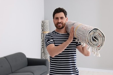 Smiling man holding rolled carpet in room