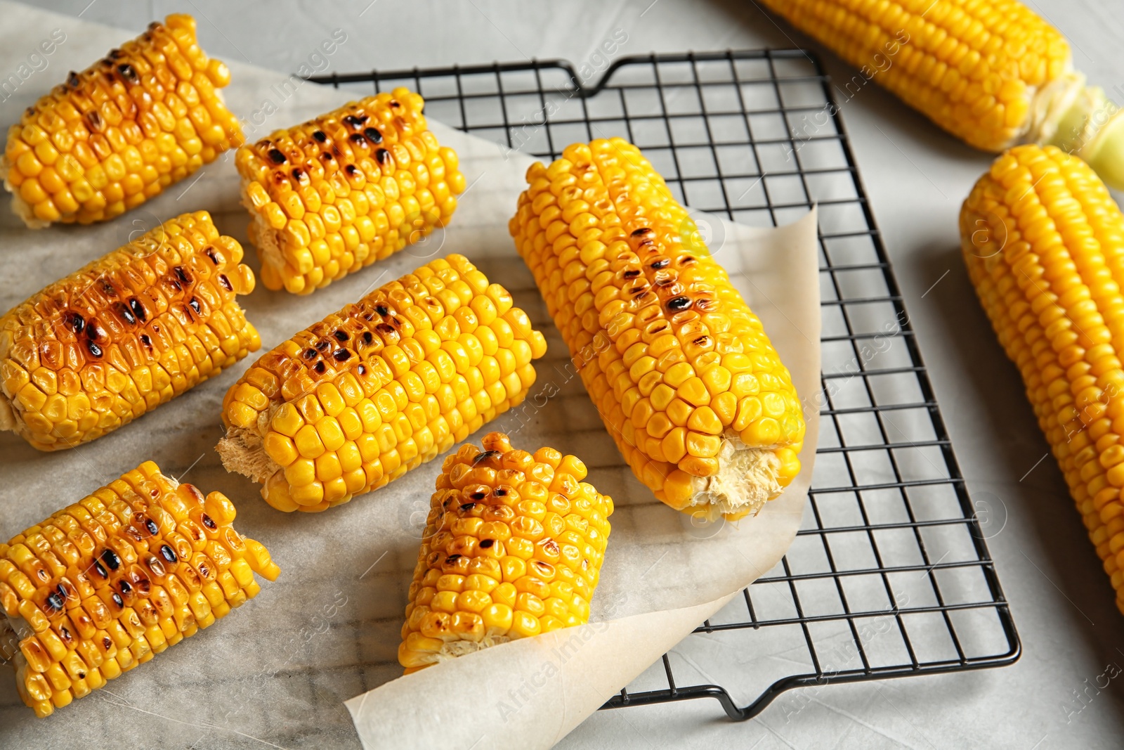 Photo of Cooling rack with grilled corn cobs on light background