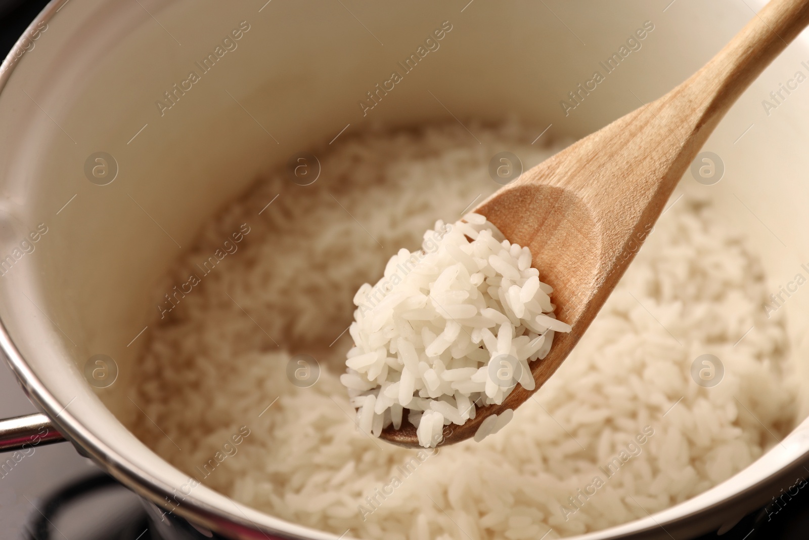 Photo of Wooden spoon with delicious rice over pot, closeup