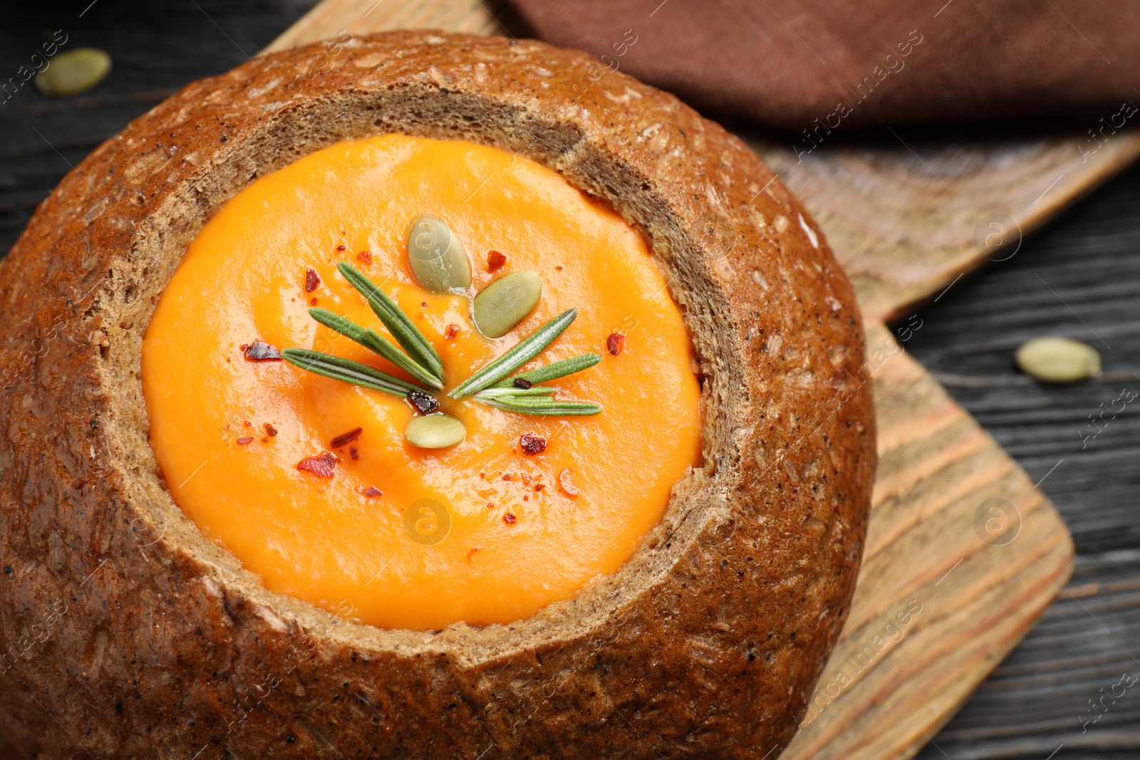 Photo of Tasty pumpkin cream soup in bread loaf on wooden board, closeup