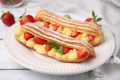 Photo of Delicious eclairs filled with cream, strawberries and mint on white wooden table, closeup