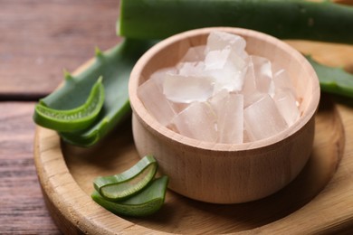 Photo of Aloe vera gel and slices of plant on wooden table, closeup