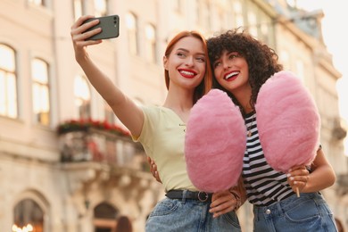 Happy friends with pink cotton candies taking selfie on city street, low angle view