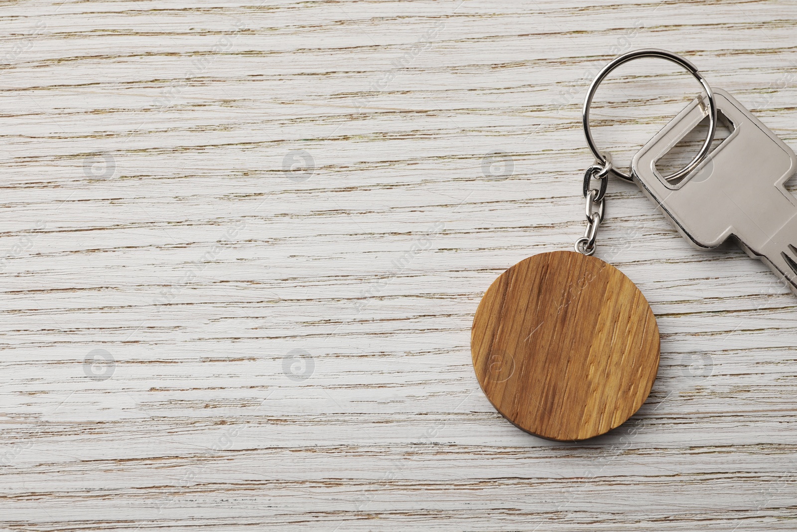 Photo of Key with keychain in shape of smiley face on light wooden background, top view. Space for text