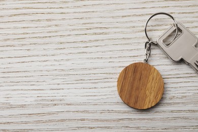 Photo of Key with keychain in shape of smiley face on light wooden background, top view. Space for text