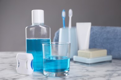 Fresh mouthwash in bottle, glass and dental floss on white marble table, closeup