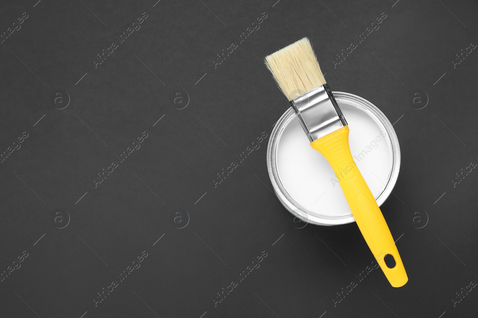 Photo of Can of white paint with brush on black background, top view. Space for text