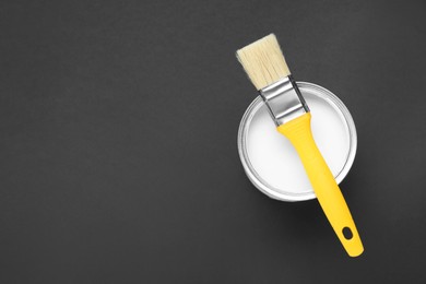 Photo of Can of white paint with brush on black background, top view. Space for text