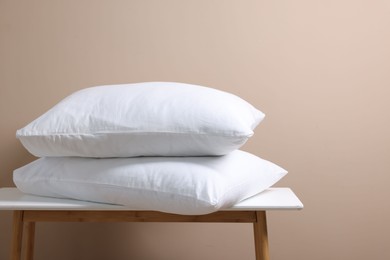 Stack of soft white pillows on table near beige wall. Space for text