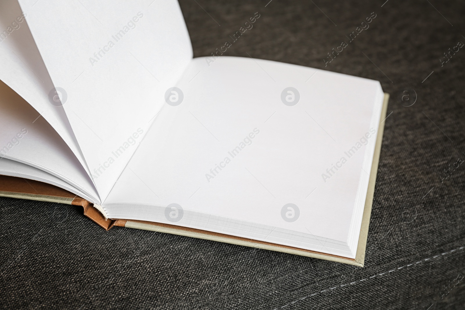 Photo of Open blank book on grey sofa, closeup view