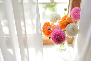 Photo of Bouquet of beautiful bright ranunculus flowers in glass vase on windowsill
