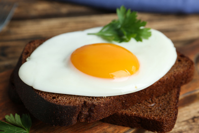Photo of Tasty fried egg with parsley and rye bread on wooden board, closeup
