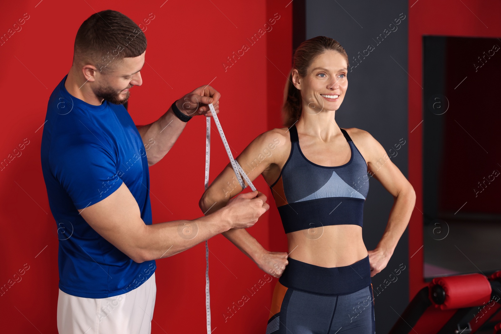 Photo of Trainer measuring woman`s triceps with tape in gym