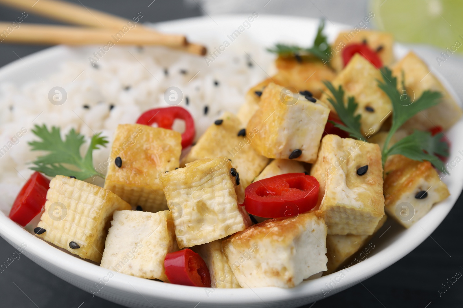 Photo of Bowl with fried tofu, rice, chili pepper and parsley on table, closeup