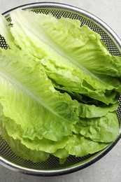 Photo of Colander with fresh leaves of green romaine lettuce on table, top view