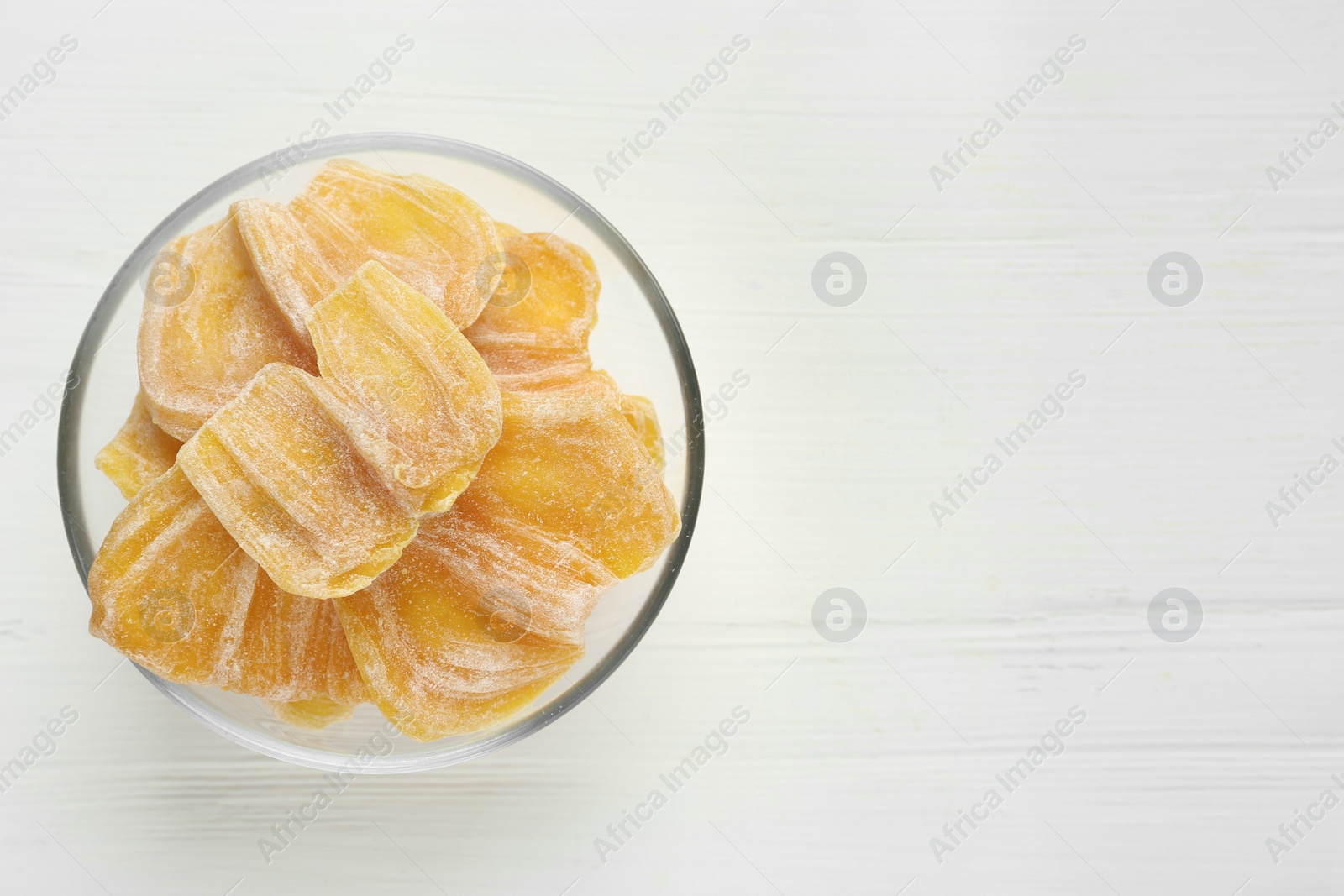 Photo of Delicious dried jackfruit slices in glass bowl on white wooden table, top view. Space for text