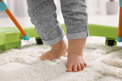 Photo of Little baby making first steps with toy walker on carpet indoors, closeup