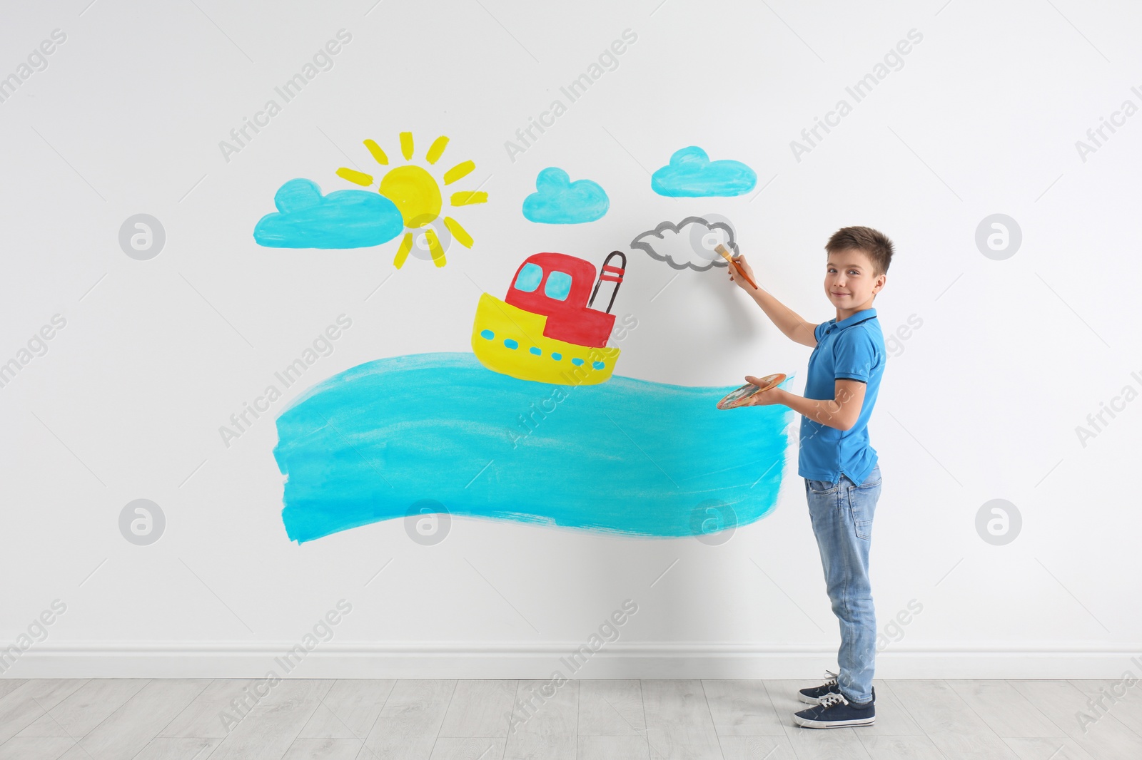 Image of Little boy drawing ship and sea on white wall indoors