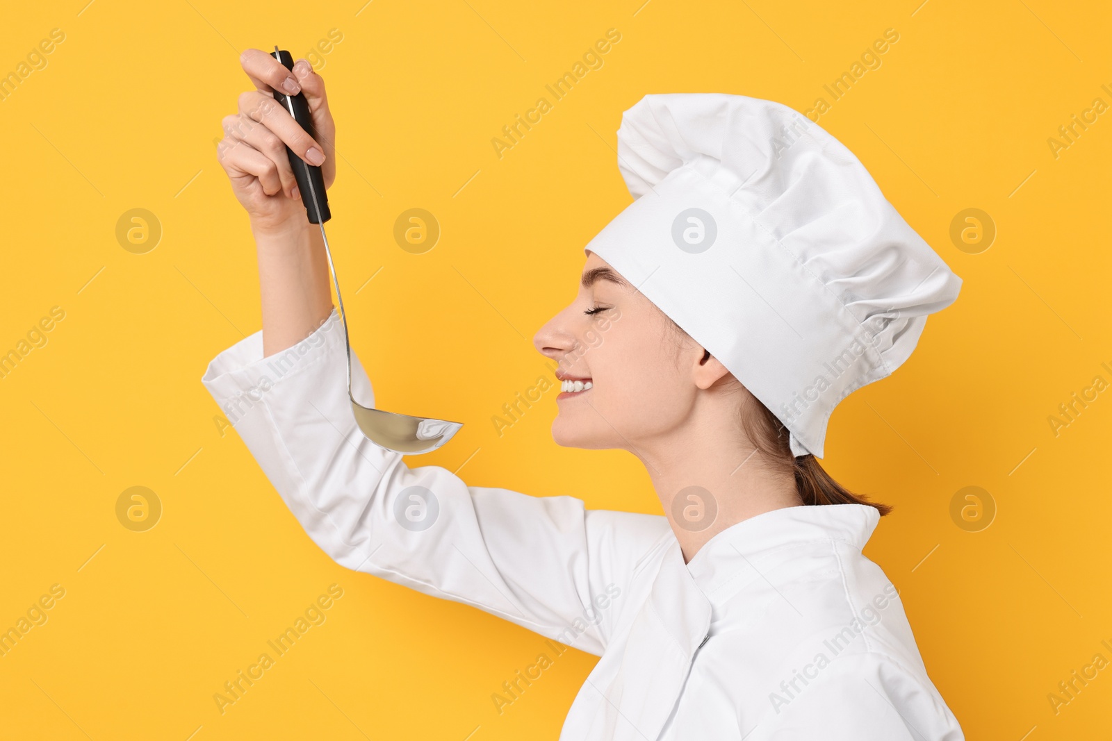 Photo of Professional chef with ladle tasting something on yellow background