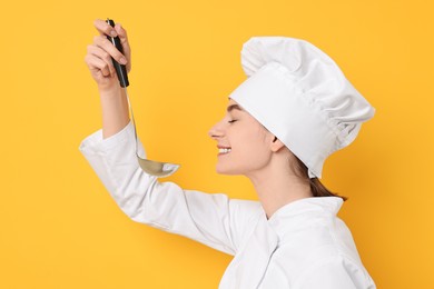 Professional chef with ladle tasting something on yellow background