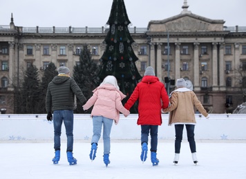 Image of Group of friends skating along ice rink outdoors, back view