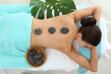 Beautiful young woman getting hot stone massage in spa salon, top view