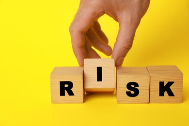 Photo of Man making word Risk with wooden cubes on yellow background, closeup