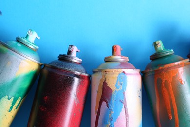 Photo of Many spray paint cans on light blue background, flat lay