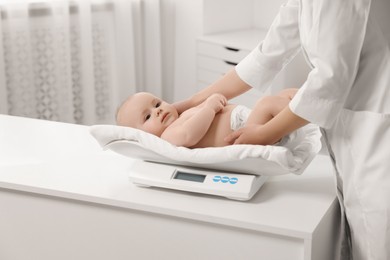 Photo of Pediatrician weighting cute little baby in clinic, closeup