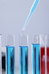 Photo of Dripping liquid from pipette into test tube on blurred background, closeup