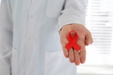 Photo of Doctor holding red awareness ribbon, closeup. World Aids day