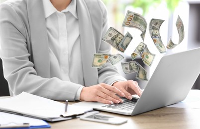 Image of Making money online. Closeup view of woman using laptop at table and flying dollars
