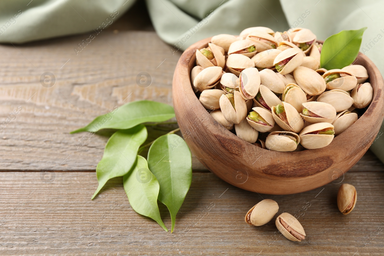 Photo of Delicious pistachios in bowl on wooden table, closeup. Space for text