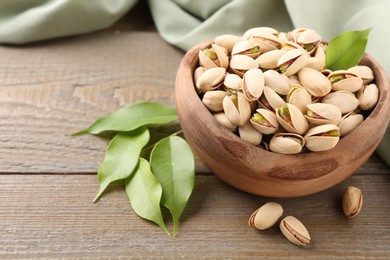 Delicious pistachios in bowl on wooden table, closeup. Space for text