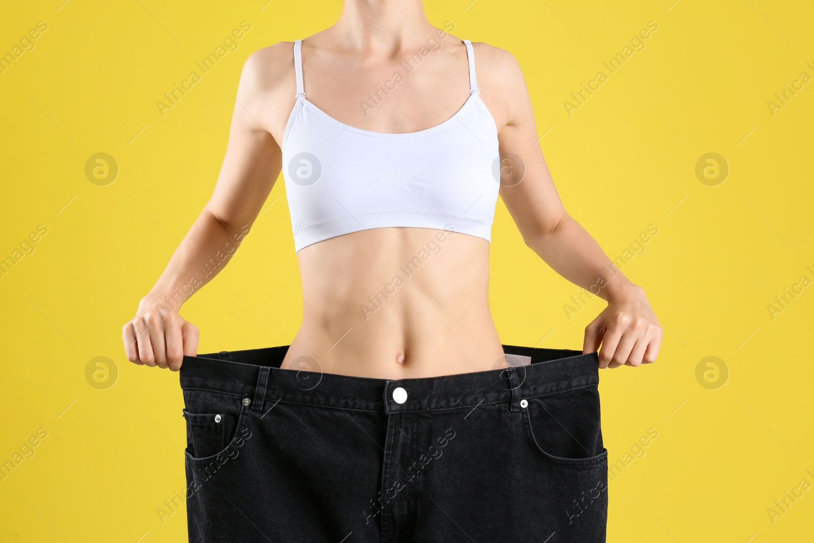 Photo of Young slim woman wearing oversized jeans on yellow background, closeup