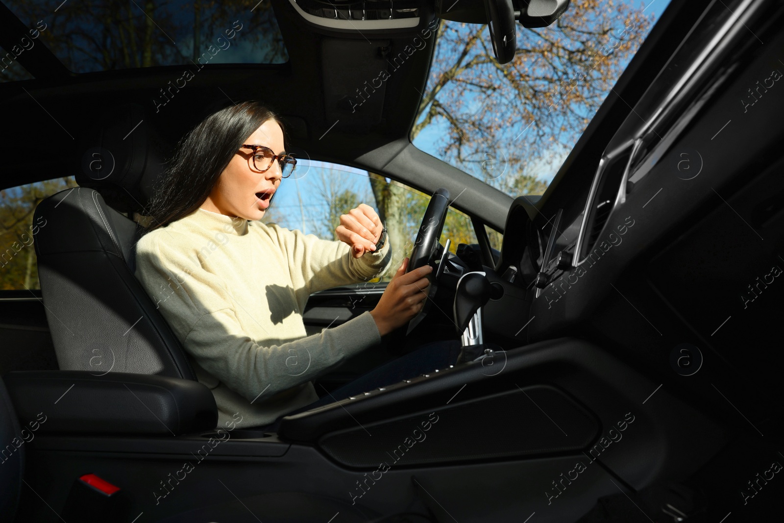 Photo of Emotional woman checking time on watch in car. Being late concept