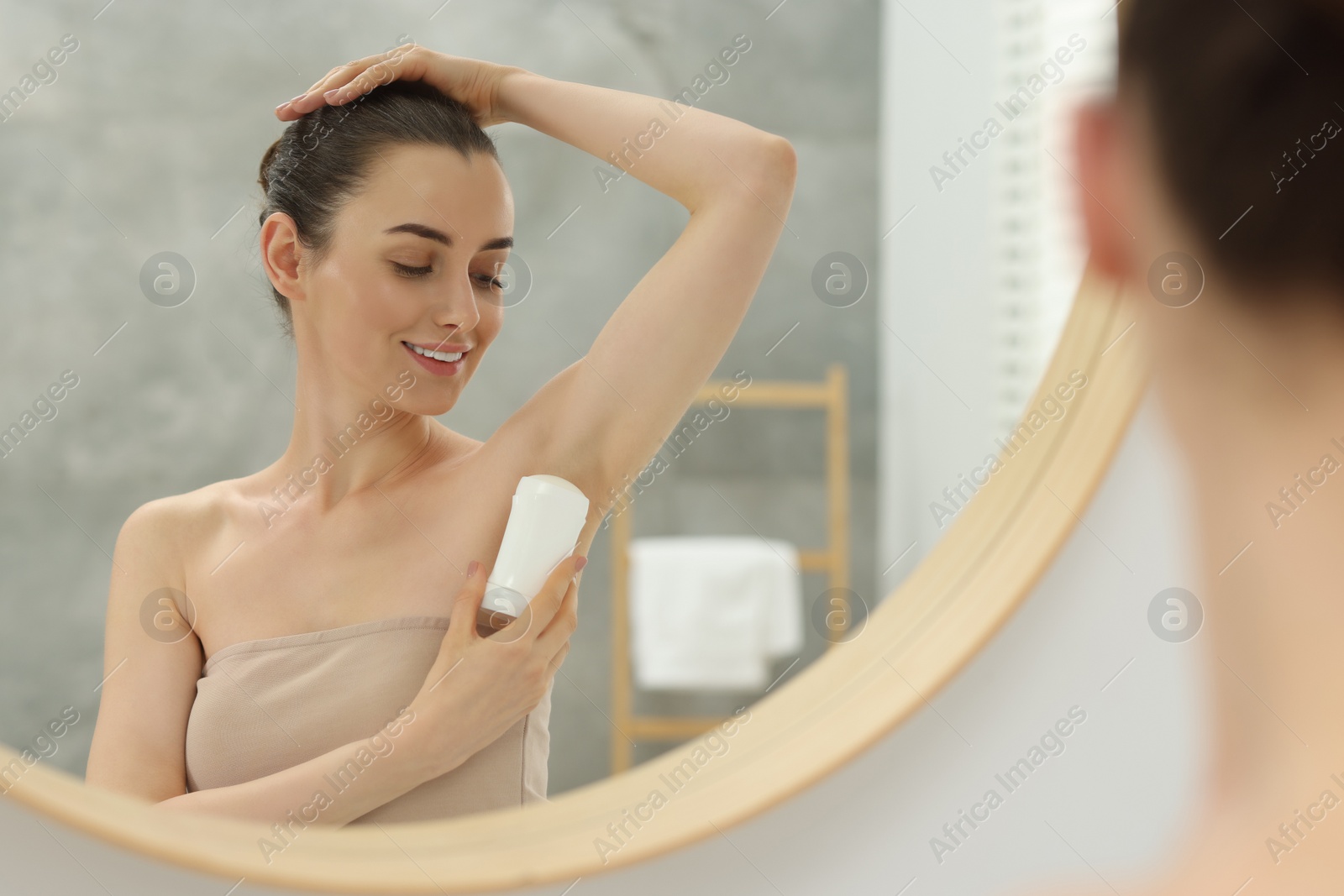 Photo of Beautiful woman applying deodorant near mirror in bathroom