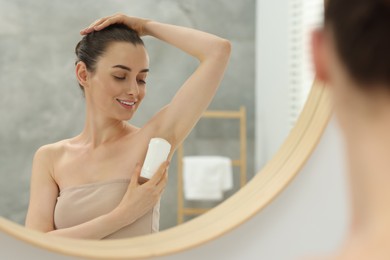 Beautiful woman applying deodorant near mirror in bathroom