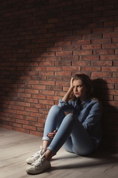 Depressed young woman sitting on floor near brick wall