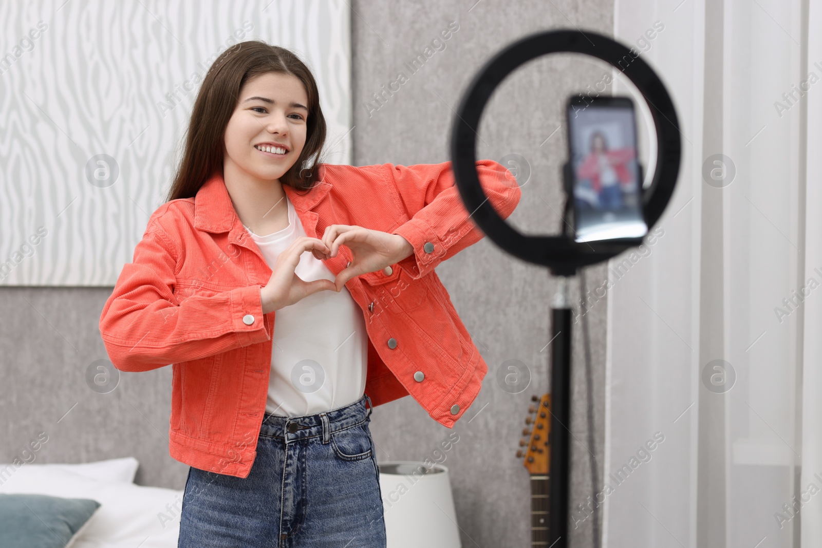 Photo of Smiling teenage blogger making heart gesture to her subscribers while streaming at home